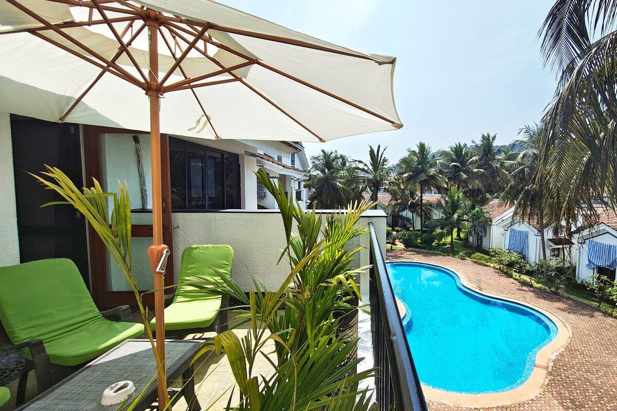 A poolside area with green lounge chairs, a white umbrella, and a clear blue pool.