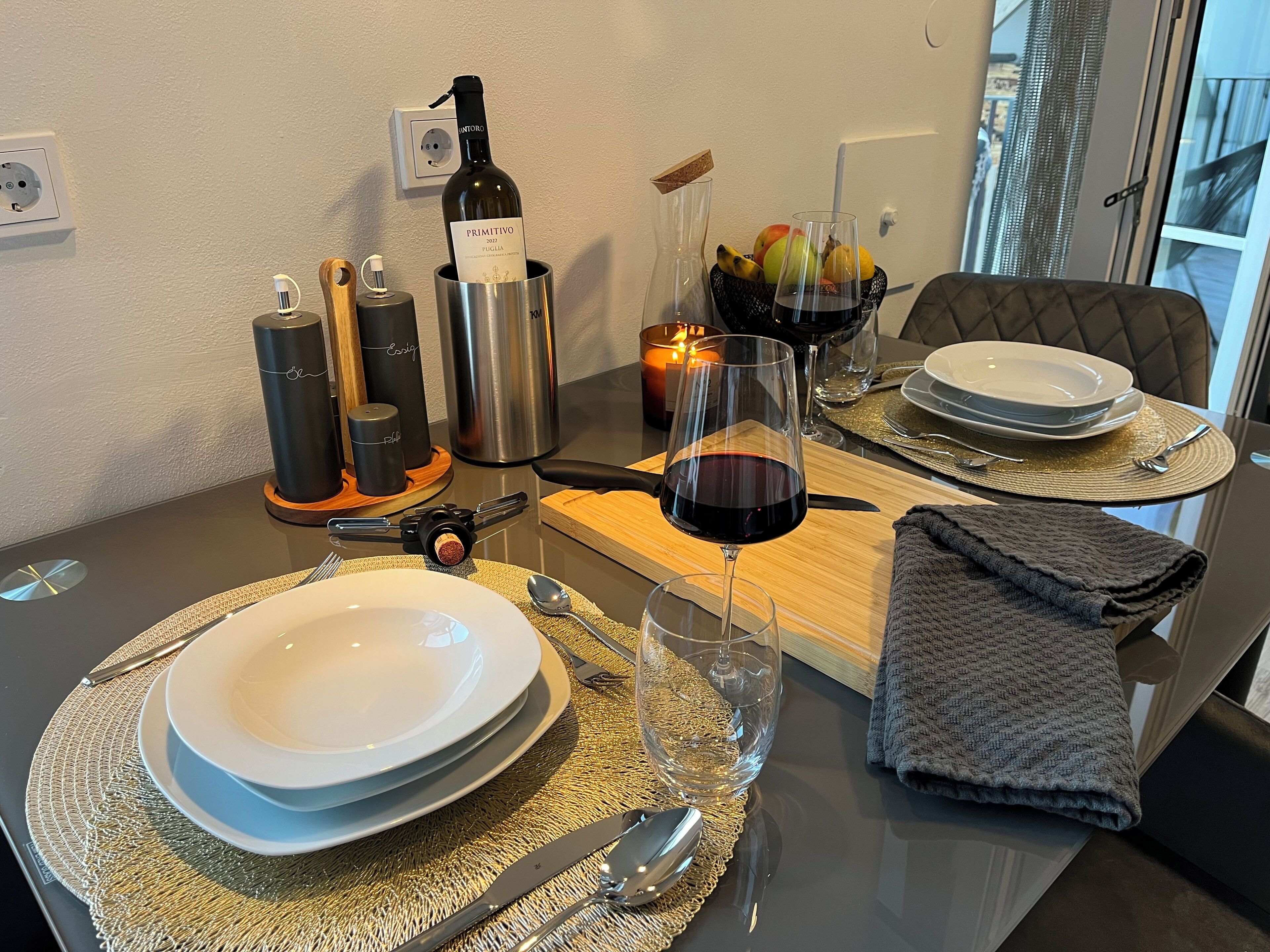 Une table à manger dressée avec des assiettes, des couverts, une bouteille de vin, des verres et une bougie.