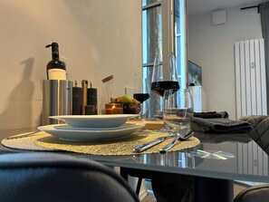 Una tavola imbandita con piatti, posate, una bottiglia e bicchieri, con una finestra e un termosifone sullo sfondo.