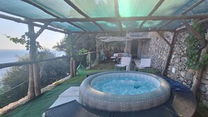 A hot tub under a pergola with a stone wall and a view of the sea.