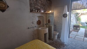 A bathroom with a stone wall, a yellow bench, two sinks, and a toilet.