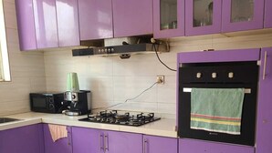 Cozinha com armários roxos, fogão a gás, micro-ondas e chaleira.