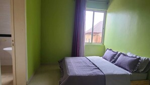 Quarto com cama, janela com cortinas, porta e tapete pequeno.