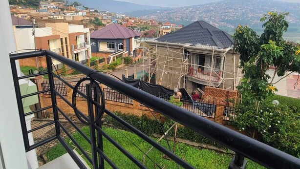 Zona residencial com casas, uma varanda com guarda-corpo de metal e vista para um horizonte urbano distante.