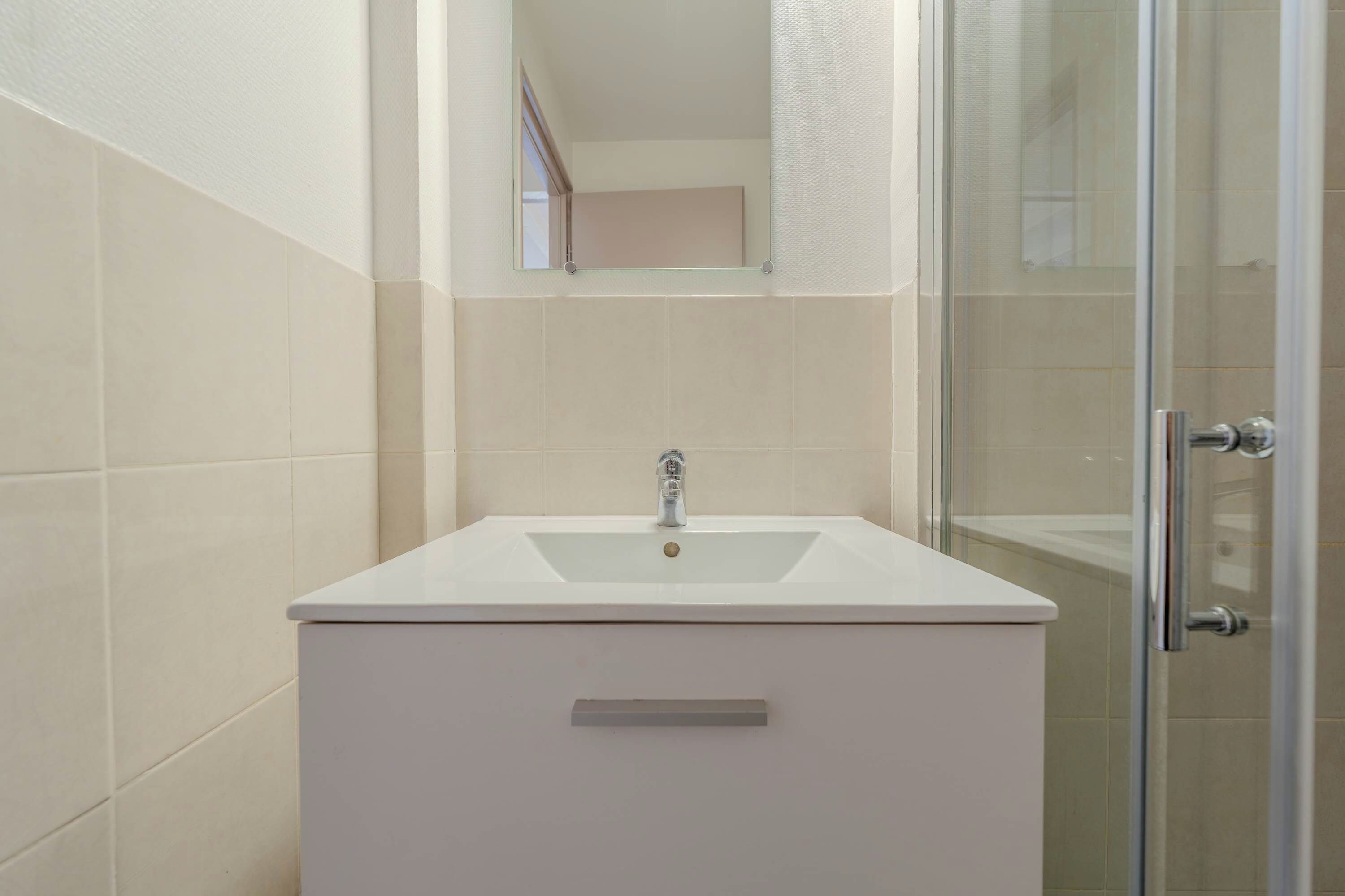 A bathroom with a white sink, a mirror, and a glass shower enclosure.