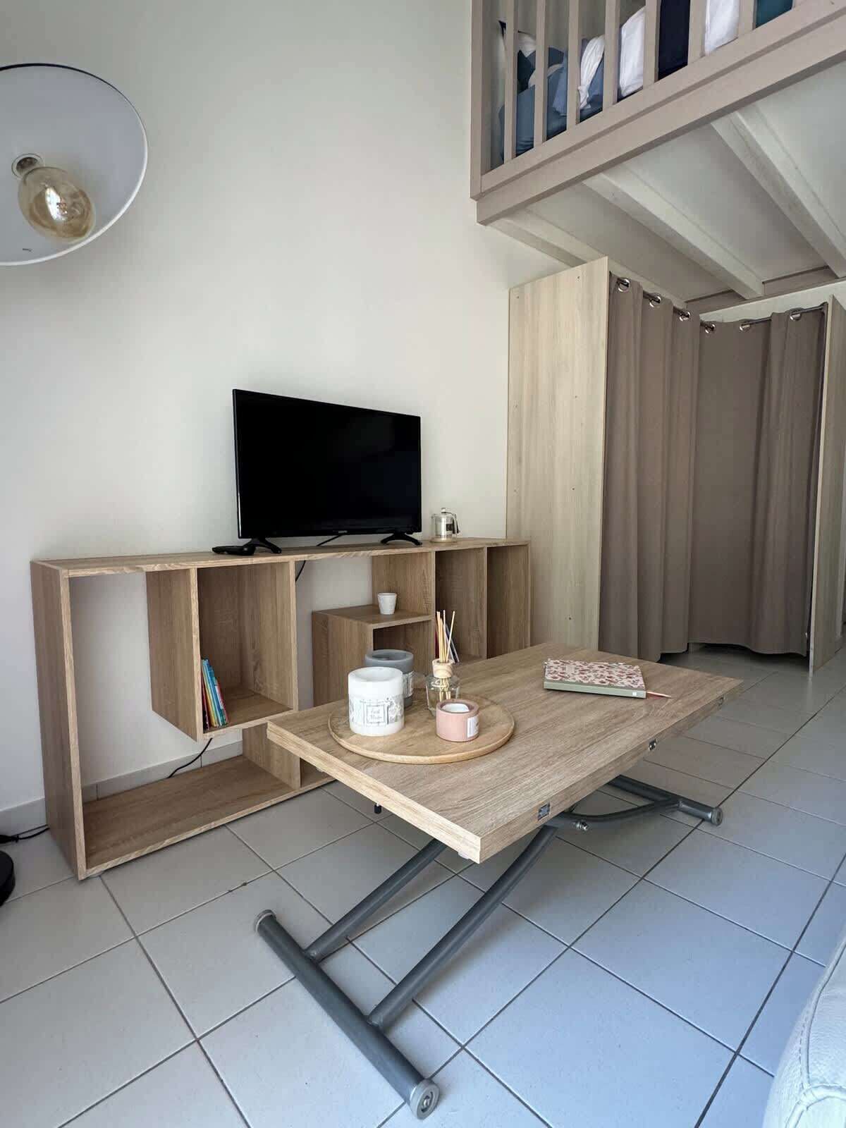 Una sala de estar moderna con un televisor de pantalla plana sobre un mueble de madera, una mesa de centro con objetos decorativos y una lámpara de techo.