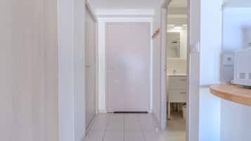 A hallway with a white door at the end, leading to a bathroom with a sink and mirror.