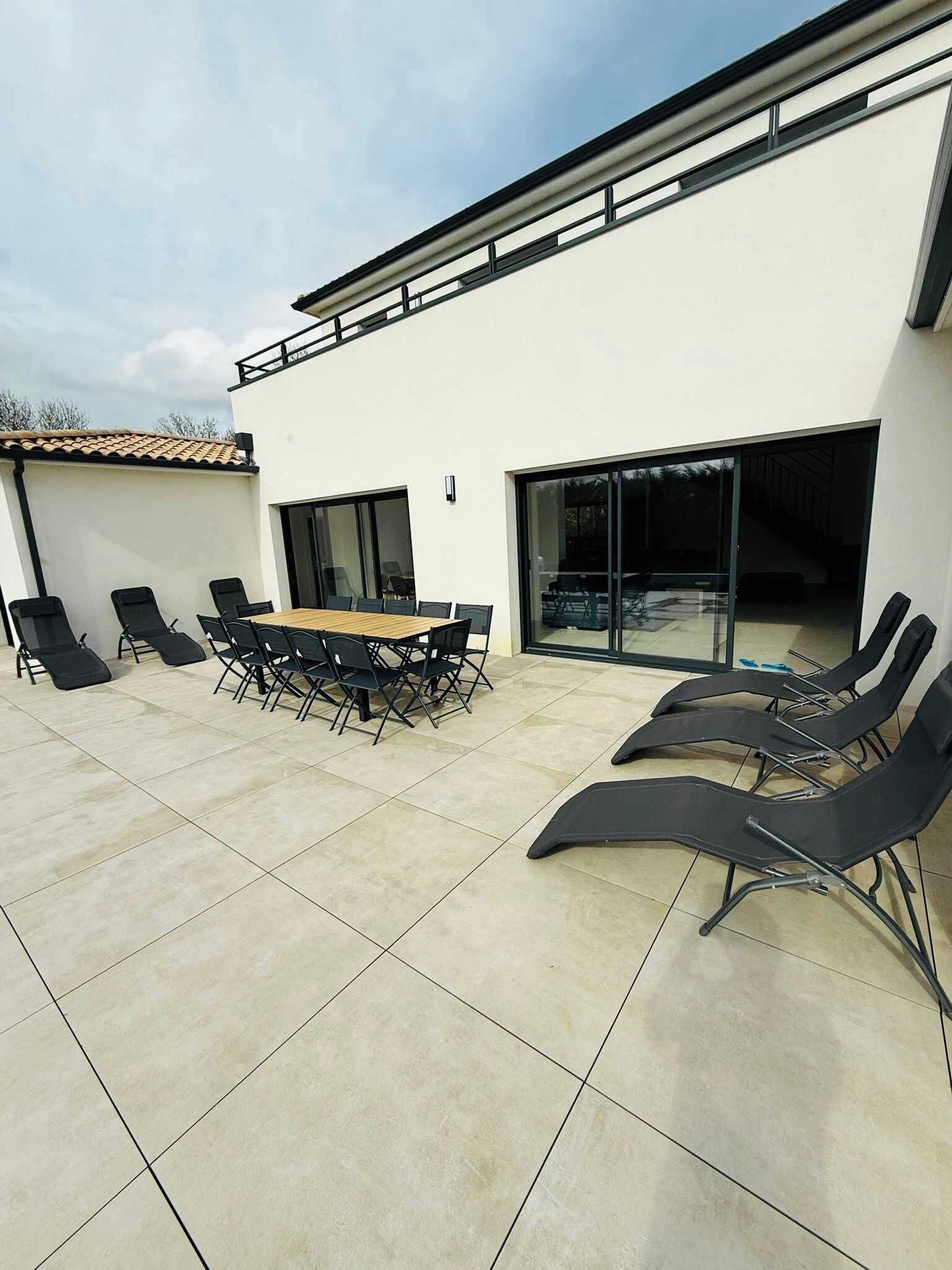 Eine Terrasse mit Tisch und Stühlen, ein überdachter Bereich und ein Gebäude mit großen Fenstern.