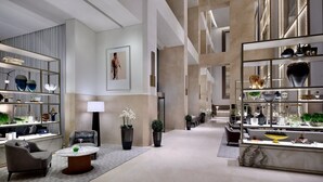 A spacious lobby with a modern design, featuring a seating area with a sofa and armchairs, a coffee table, and a large display of decorative items on shelves. - Emaar Fashion Avenue Residences  (Dubai)