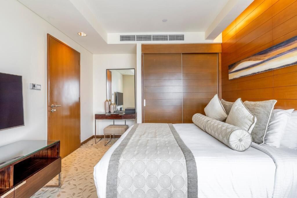 A modern hotel room with a large bed, a TV, a desk, and a wardrobe.