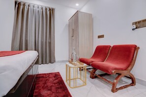Una habitación de hotel con una cama, una silla roja, una mesita y un armario.