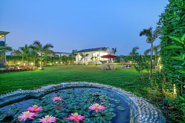 A well-maintained garden with a pond, palm trees, and a building in the background.