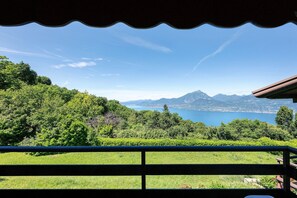 Un balcón con vistas a un lago, montañas y exuberante vegetación.