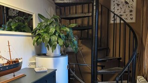 Een kleine kamer met een donkerblauwe kast, een model schip, een plant in pot, een wenteltrap en een poster met vogels.