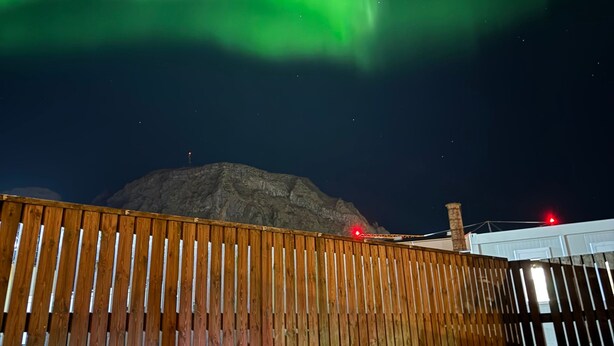 Een houten terras met zitplaatsen, een berg op de achtergrond en het Noorderlicht aan de hemel.