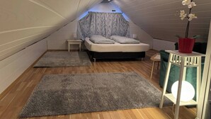 Een kleine kamer met schuin dak, een bed, nachtkastje, een bloempot en een tafeltje met lamp.