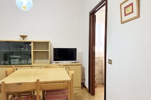 A dining area with a wooden table and chairs, a television on a stand, a glass cabinet with kitchen items, and a door leading to another room. - SE218 - Senigallia, comfortable one-bedroom apartment nearby the sea (Senigallia)