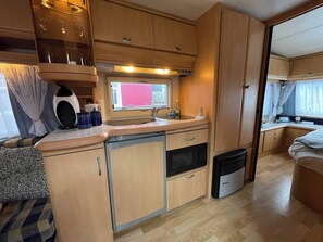 Une cuisine compacte pour camping-car, dotée de meubles en bois, d’un évier, d’une cuisinière et d’un lave-vaisselle de petite taille.