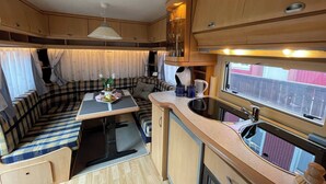 A compact RV kitchen with a dining area, a sink, and a window. - The Cozy Caravan Vestmannaeyjar (Vestmannaeyjar)