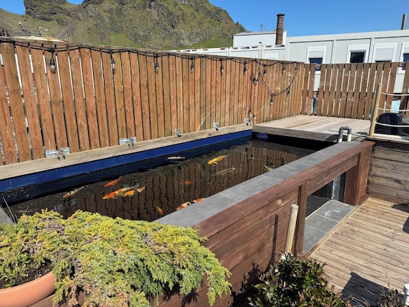 Un bassin à carpes koï, agrémenté d’une terrasse en bois et surplombant un paysage montagneux.