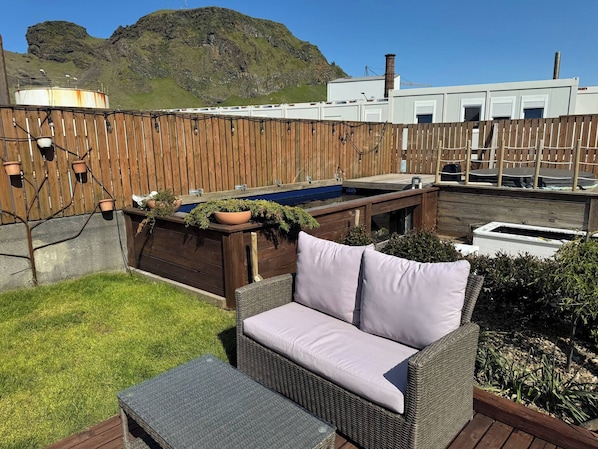 Un espace patio aménagé avec un canapé en osier et une petite table, entouré d’une terrasse en bois et d’une clôture en bois.