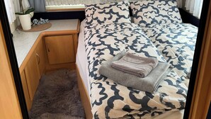 A compact bedroom with a bed, a small table, and a potted plant. - The Cozy Caravan Vestmannaeyjar (Vestmannaeyjar)