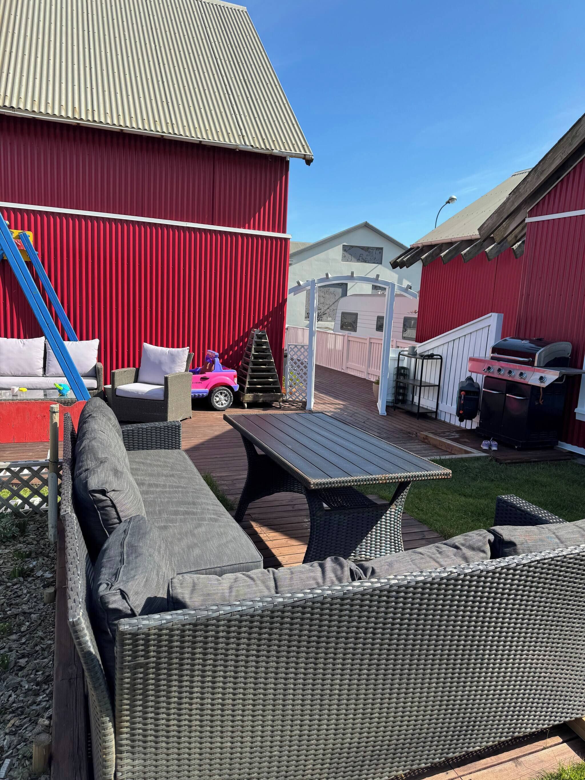 A patio area with wicker furniture, a children's ride-on toy, a barbecue grill, and a red barn in the background.