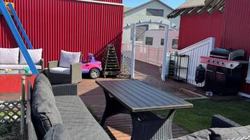 A patio area with wicker furniture, a children's ride-on toy, a barbecue grill, and a red barn in the background.