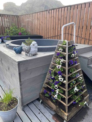 A wooden deck with a tiered planter filled with flowers, a bird sculpture, and a small pond. - The Cozy Caravan Vestmannaeyjar (Vestmannaeyjar)