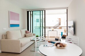 Uma sala de estar moderna com um sofá, uma mesa de jantar com uma tigela de petiscos e uma TV fixada na parede.