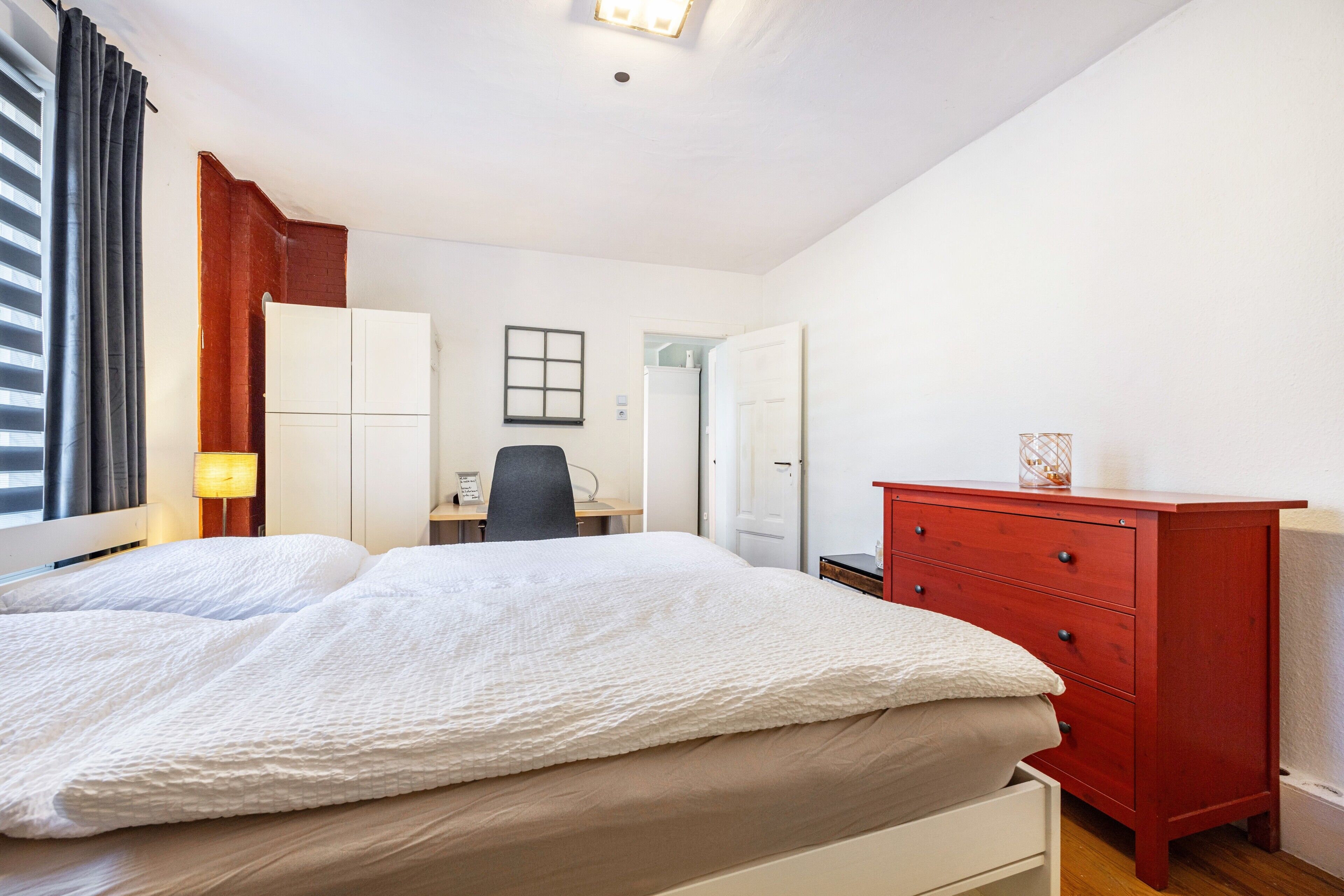 Una camera da letto con un letto, una scrivania, una sedia, un comò e una finestra con tende.