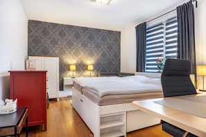 Un dormitorio con cama, mesitas de noche, escritorio, silla, armario y ventana con cortinas.