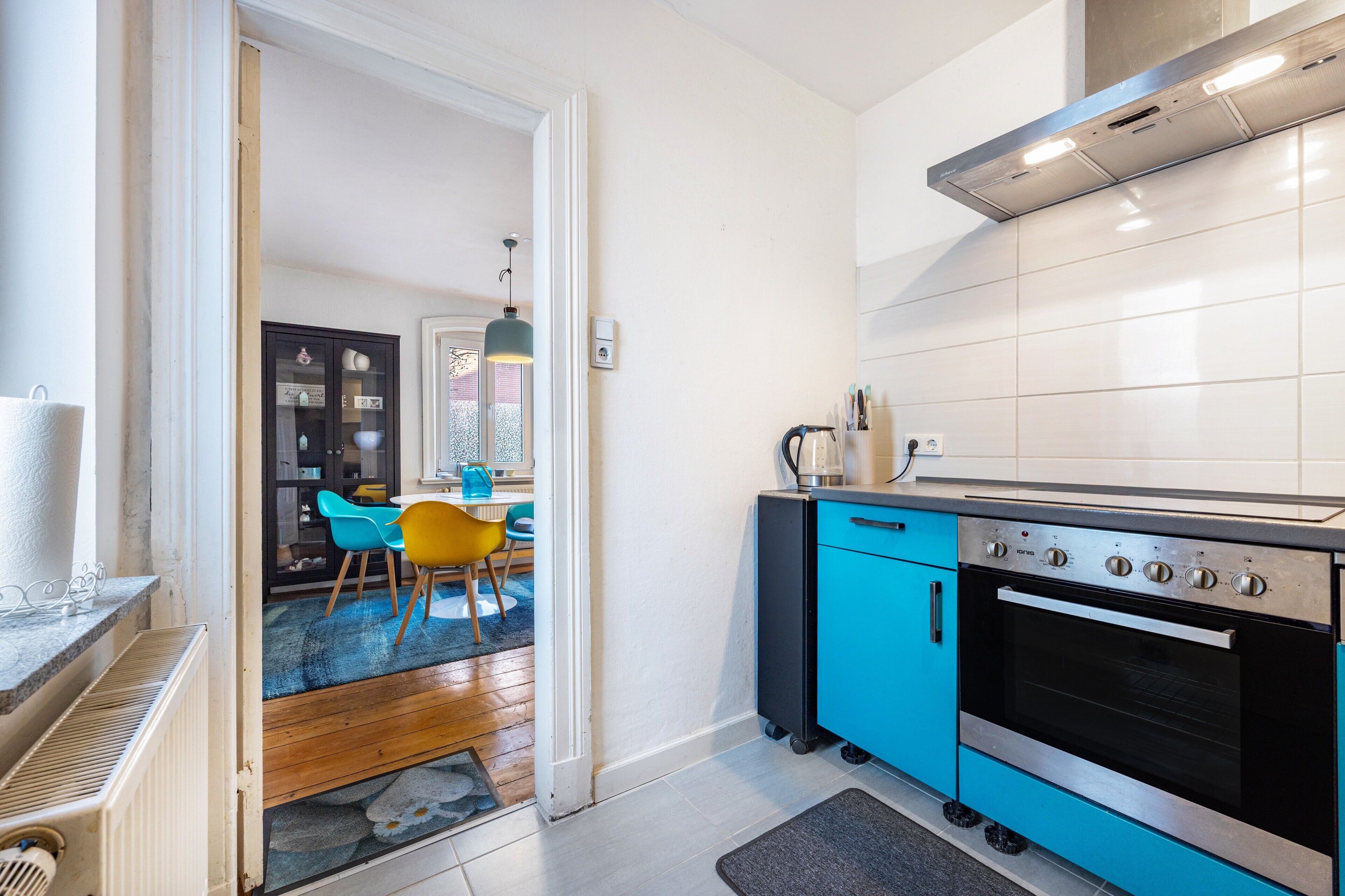 Una cocina moderna con horno empotrado, un mueble azul y un comedor con sillas.