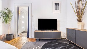 Moderni olohuone, jossa on litteänäyttöinen televisio, puulattia, harmaa sohva, musta sohvapöytä ja ruukkukasvi.