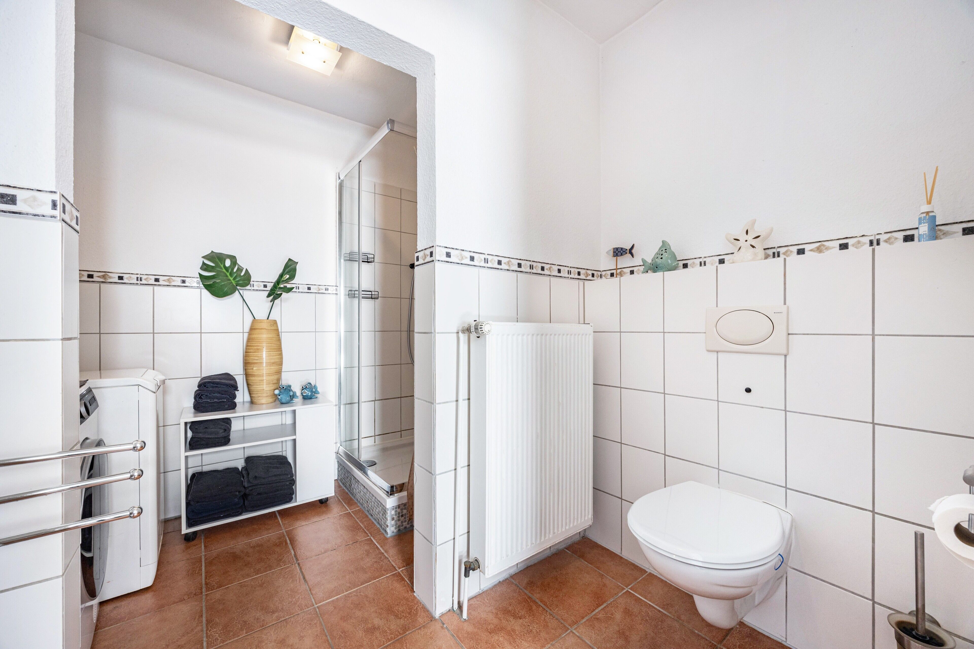 Ein Badezimmer mit Toilette, Duschkabine, Handtuchhalter und Ablage mit gefalteten Handtüchern.