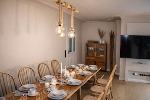 Een eetkamer met een houten tafel voor zes personen, omringd door houten stoelen. Achterin staat een houten kast met glazen deuren, en aan de muur is een flatscreen televisie bevestigd.