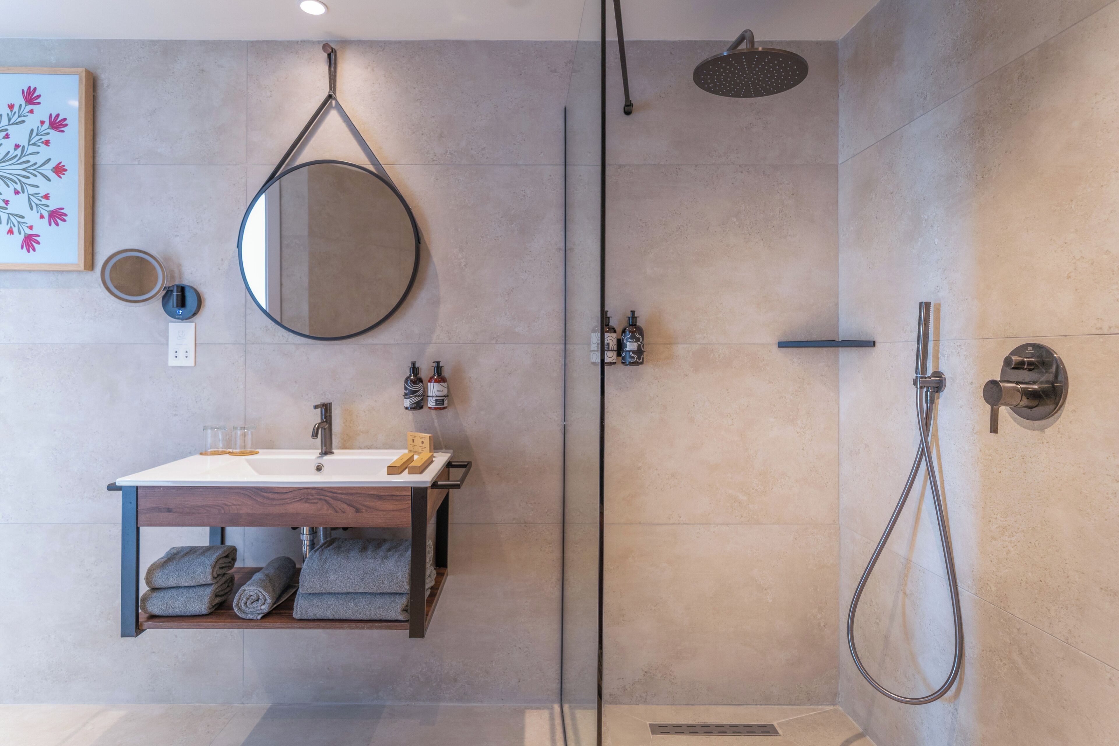 Un baño moderno con ducha envuelta en vidrio, tocador de madera con lavamanos y espejo.