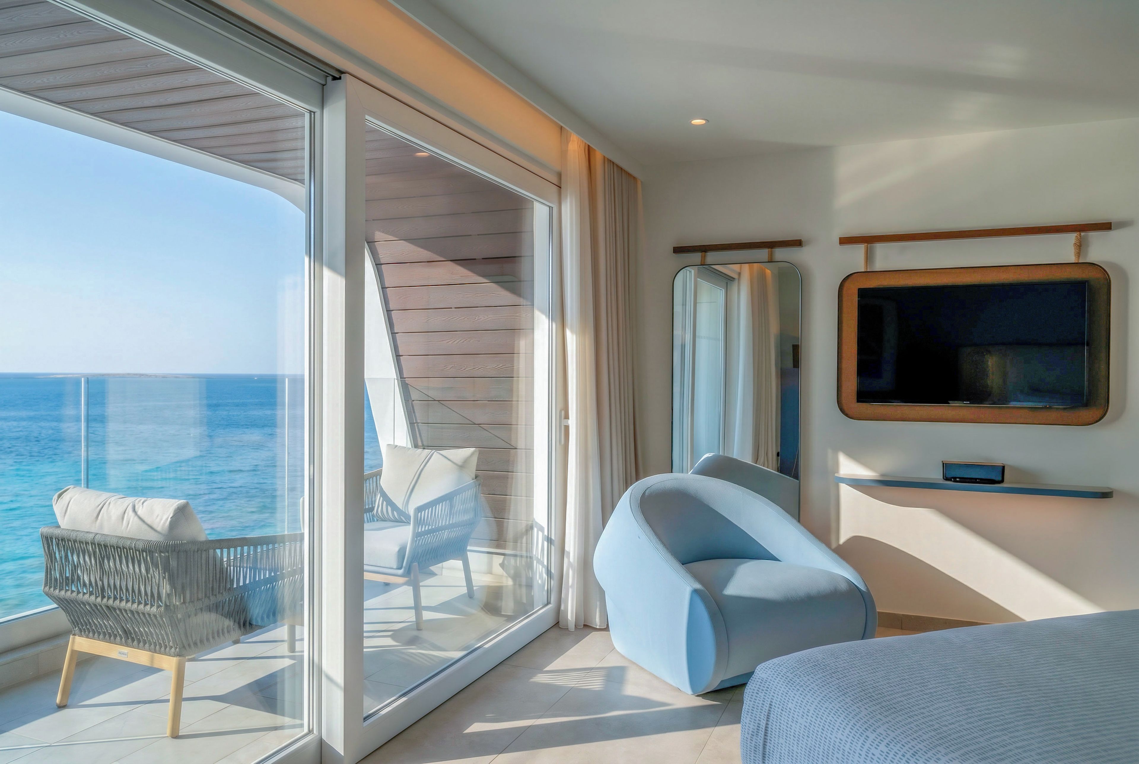 A balcony with a view of the sea, a chair, a sofa, and a television on the wall.