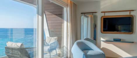 A balcony with a view of the sea, a chair, a sofa, and a television on the wall.