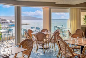 A dining area with wicker chairs and tables, overlooking a body of water with a distant shoreline. - Innside By Meliá Bugibba (St. Paul's Bay)