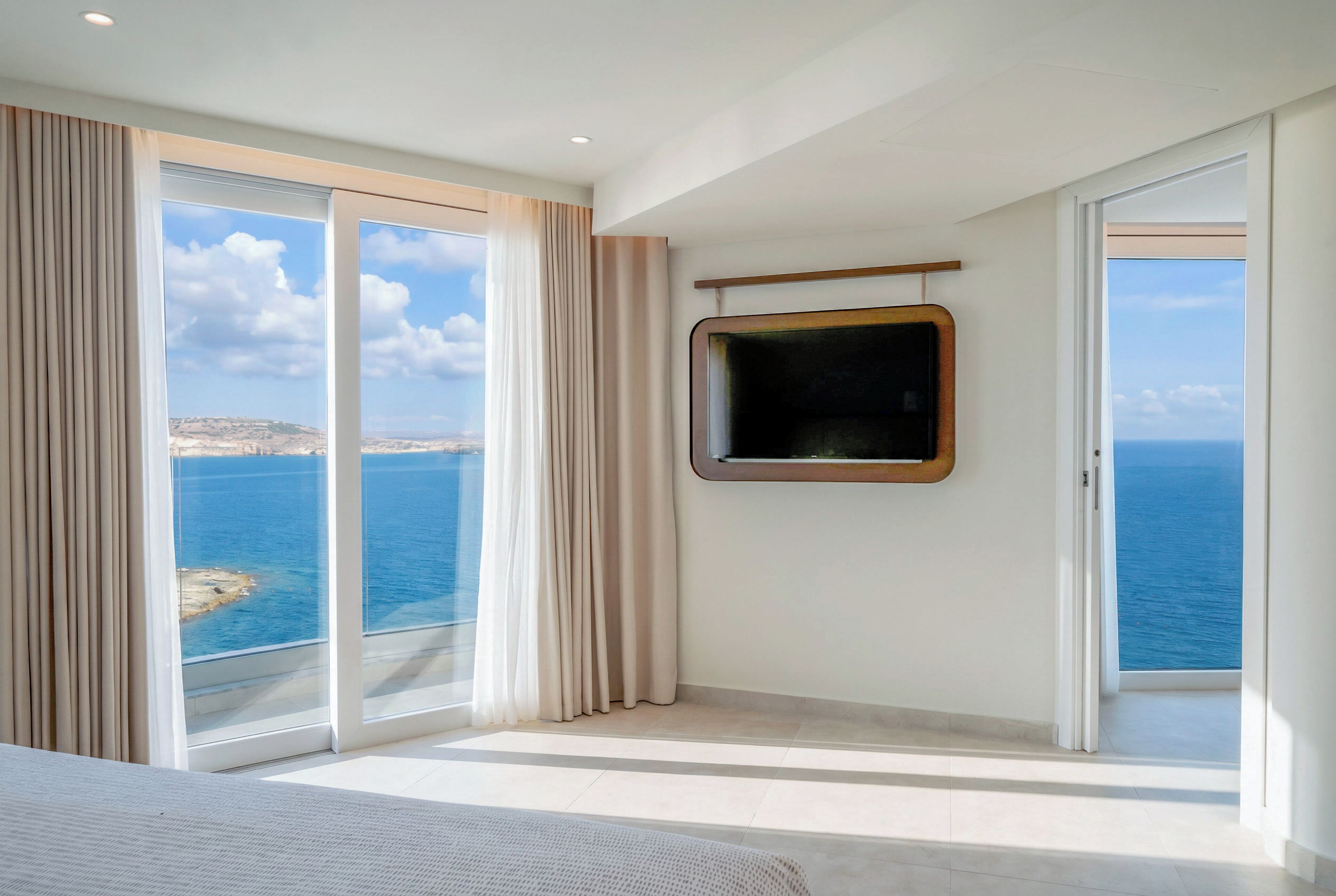 A room with a large window, a bed, and a flat-screen TV mounted on the wall.