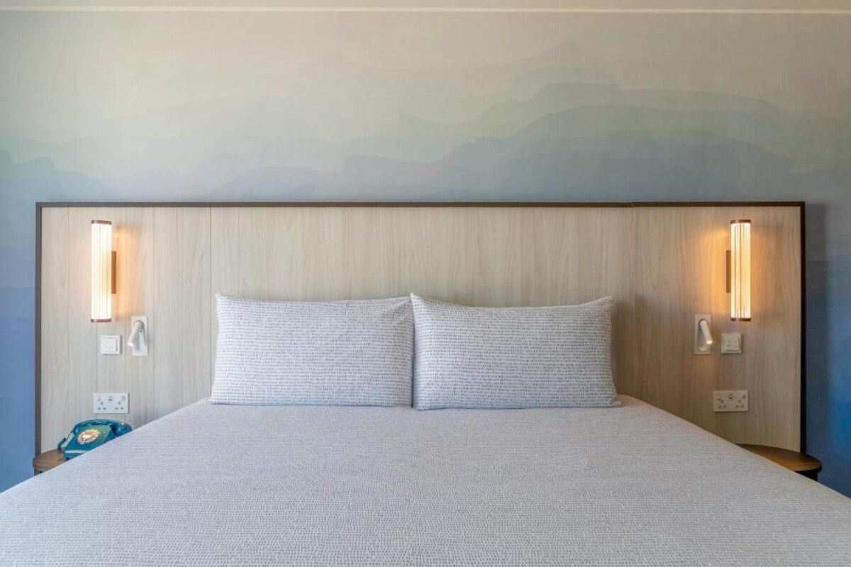 A hotel room with a large bed, two bedside lamps, and a wall-mounted telephone.