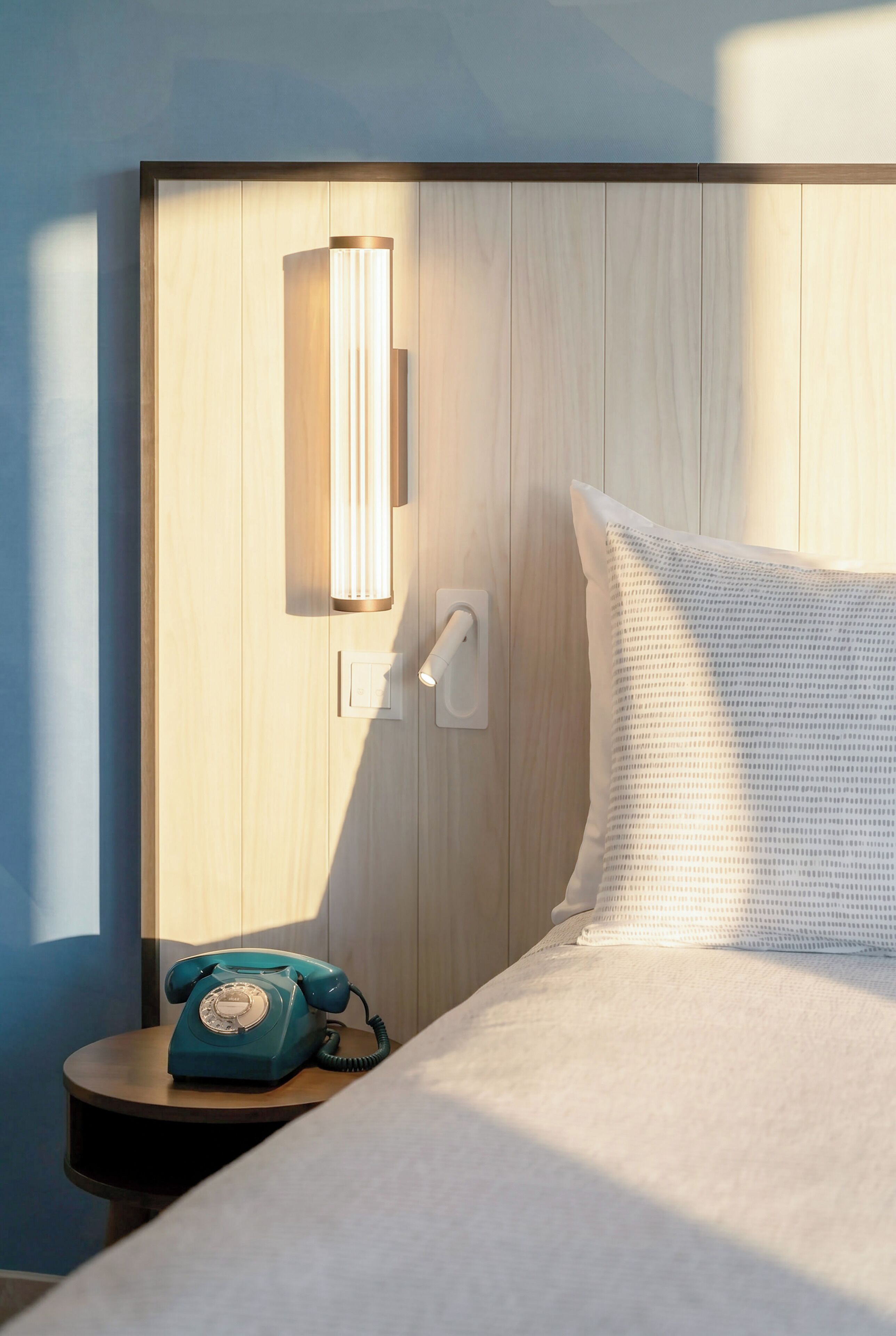 Una habitación de hotel con cabecera de madera, teléfono en la mesita de noche y almohada blanca.