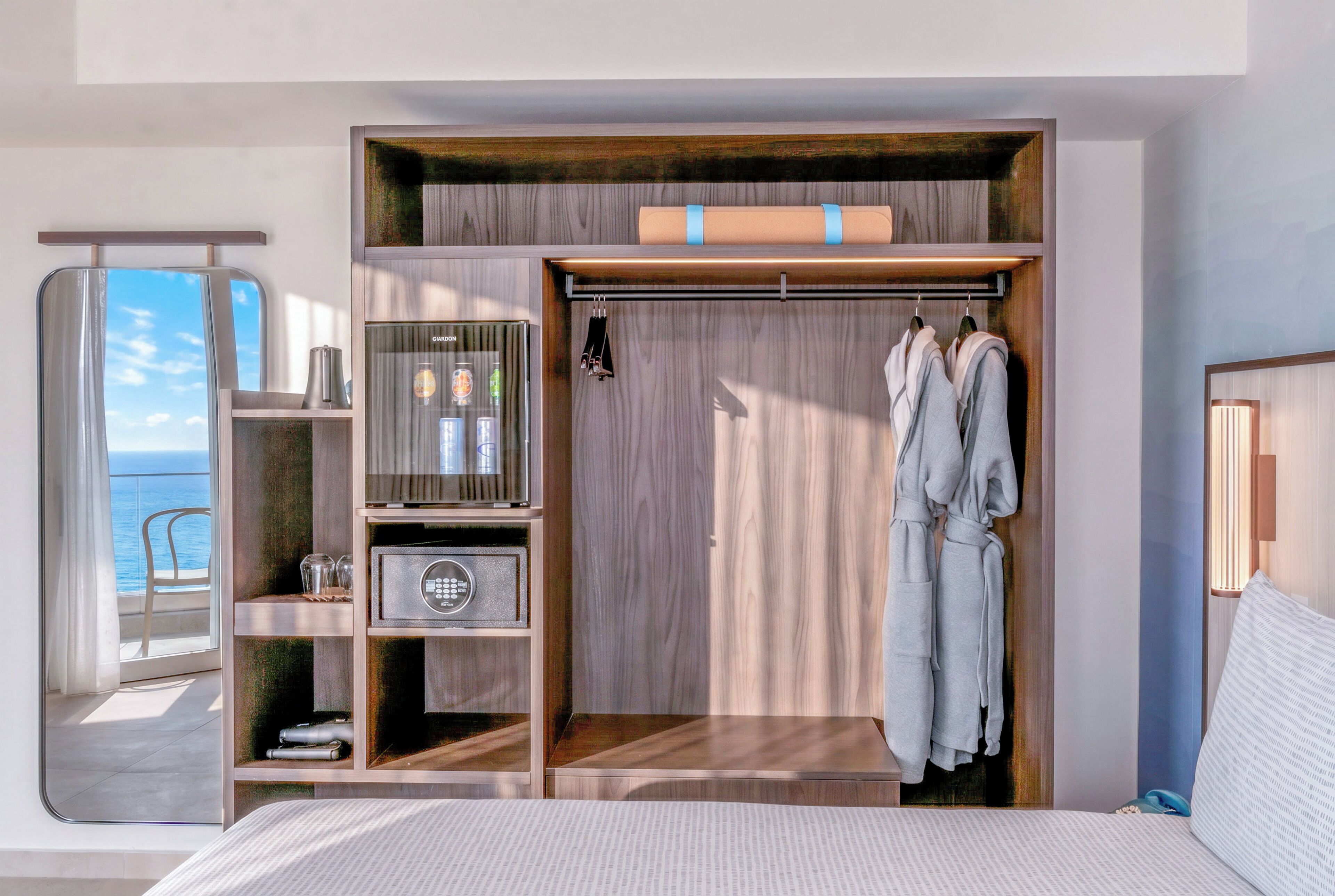 A bedroom with a built-in closet, a minibar, a safe, and a view of the sea.