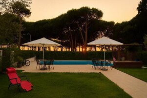 Un área de piscina con dos sombrillas, una silla de descanso roja y una terraza con sillas y una mesa.