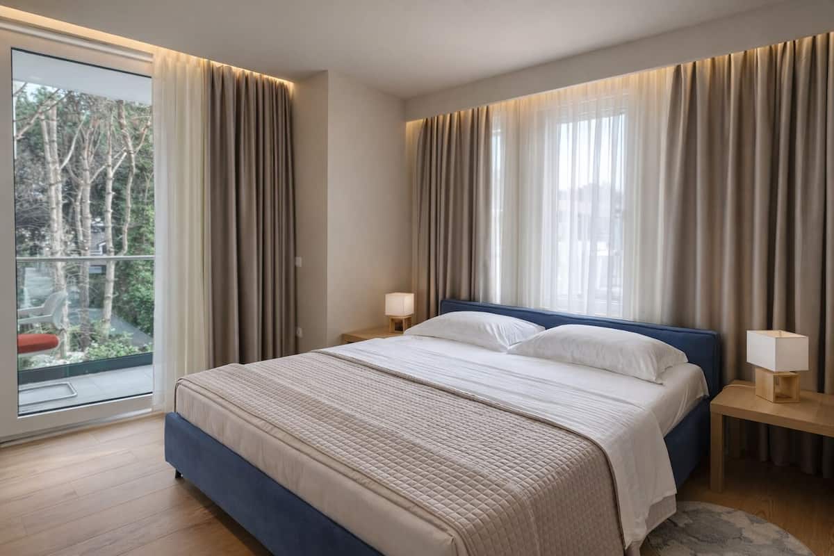 Un dormitorio con una cama grande, dos mesitas de noche y vistas por la ventana.