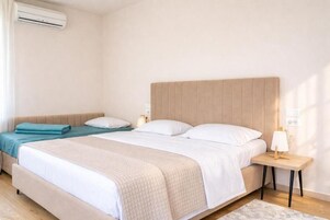 Un dormitorio con una cama grande, una cama más pequeña, una mesita de noche con una lámpara y un equipo de aire acondicionado en la pared.