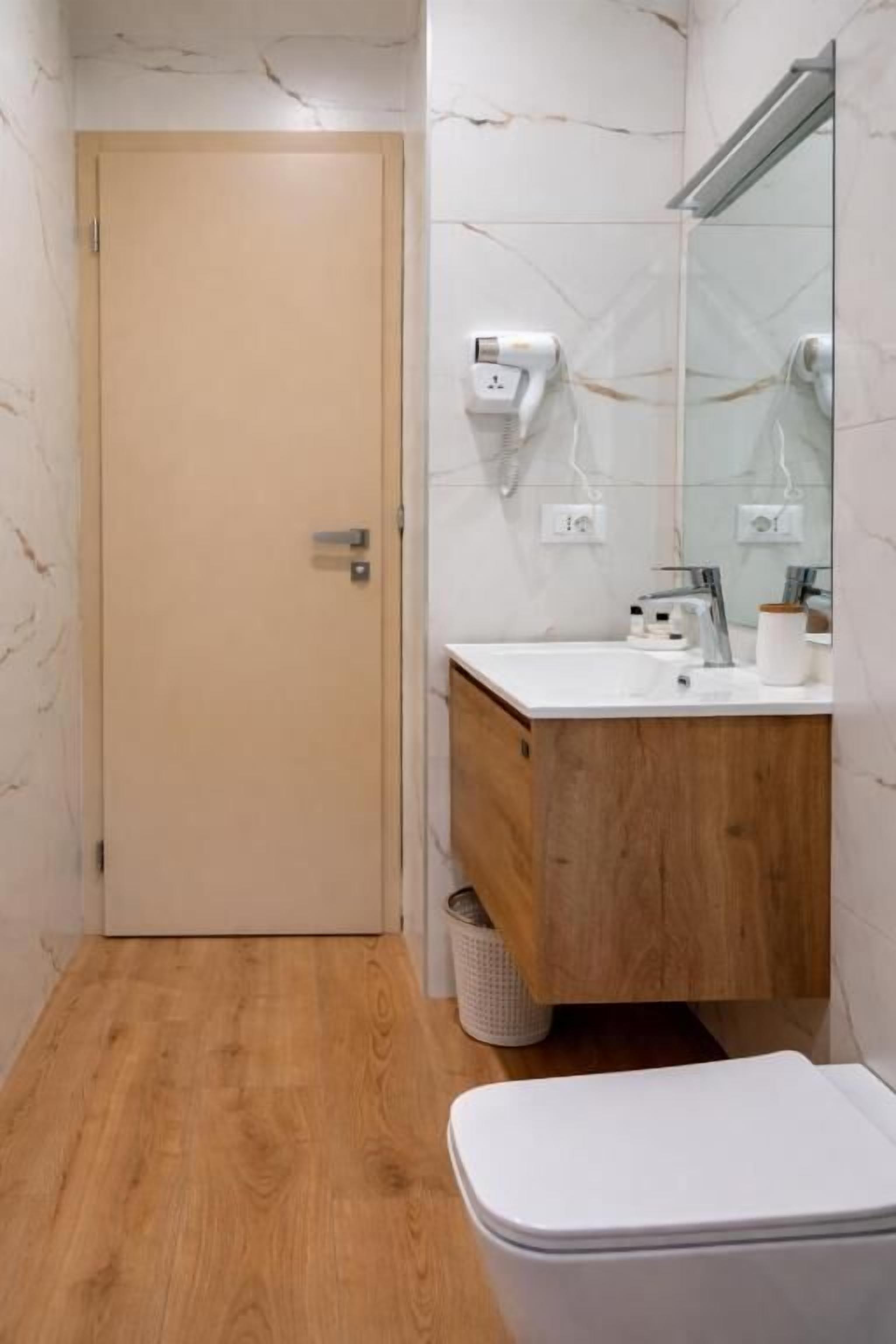 A bathroom with a wooden floor, a white toilet, a wooden vanity, a mirror, and a towel rack.