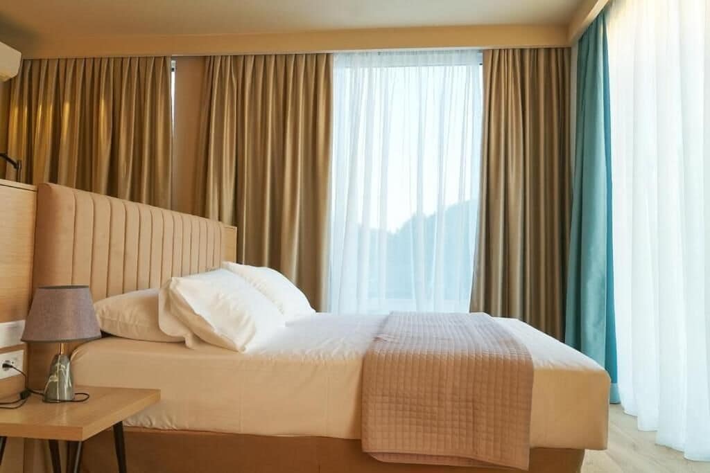 Een hotelkamer met een bed, nachtkastje met een lamp en gordijnen.
