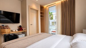 A hotel room with a bed, a television, a small kitchenette, a balcony with a chair, and a window with curtains. - Vila Eva (Golem)